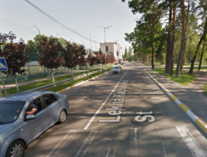 Widok ulicy. Po lewej jeden samochód. Po prawej park