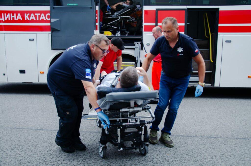 Ratownicy PCPM przenoszą rannego pacjenta z Ukrainy na noszach z ukraińskiego autobusu medycznego podczas ewakuacji medycznej